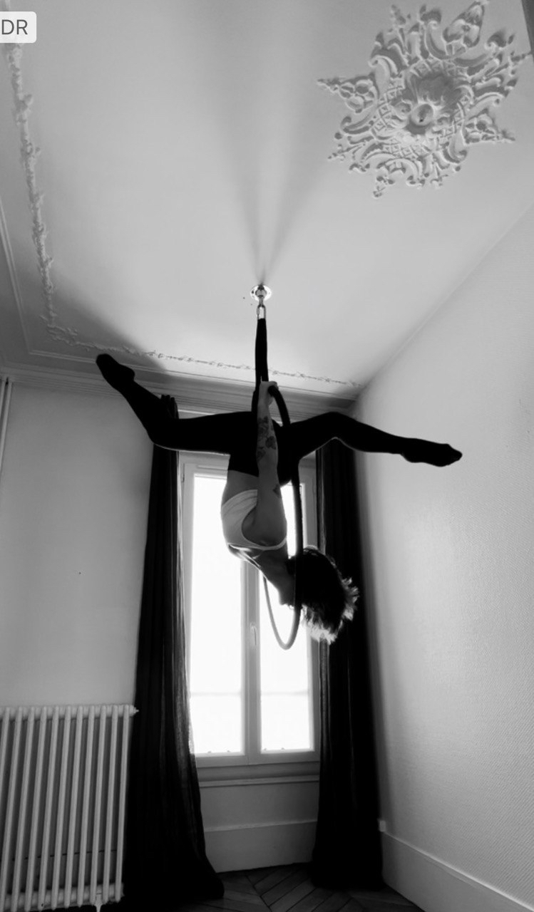 Photo en noir et blanc d'Emma faisant une pose la tête en bas s'agrippant à son cerceau aérien.